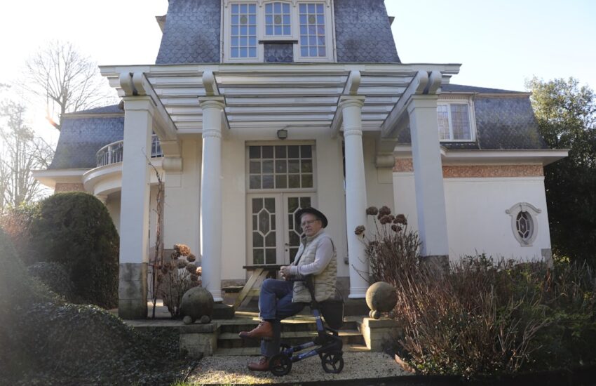 Elderly man sits on a walker outside a large house